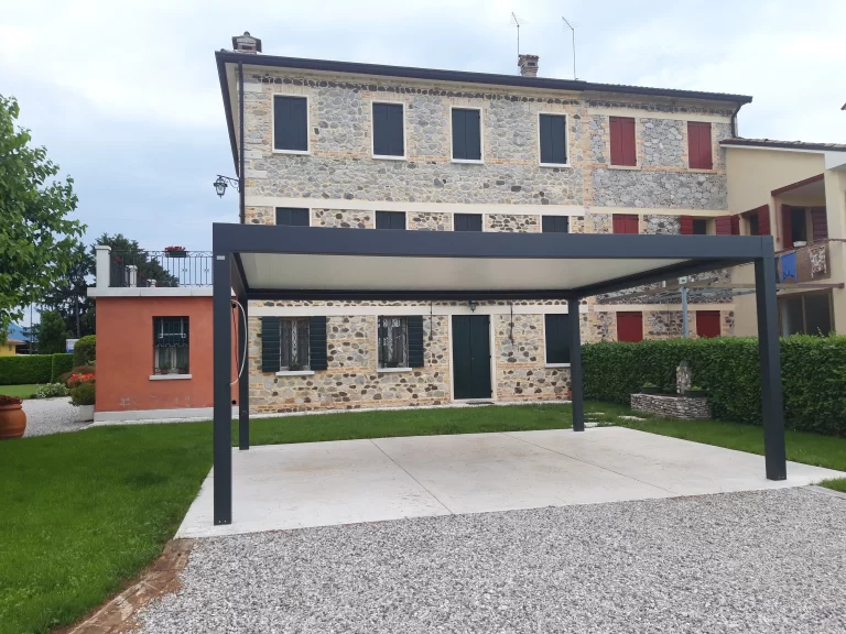Pergola bioclimatica con lamelle orientabili davanti a una casa in pietra