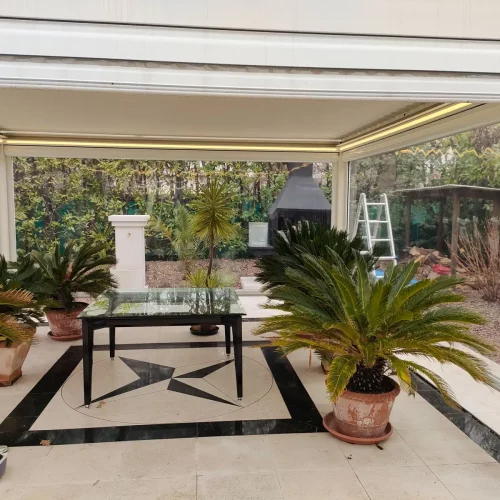 Spazio esterno con piante sotto un a pergola chiusa lateralmente da vetrotende zip