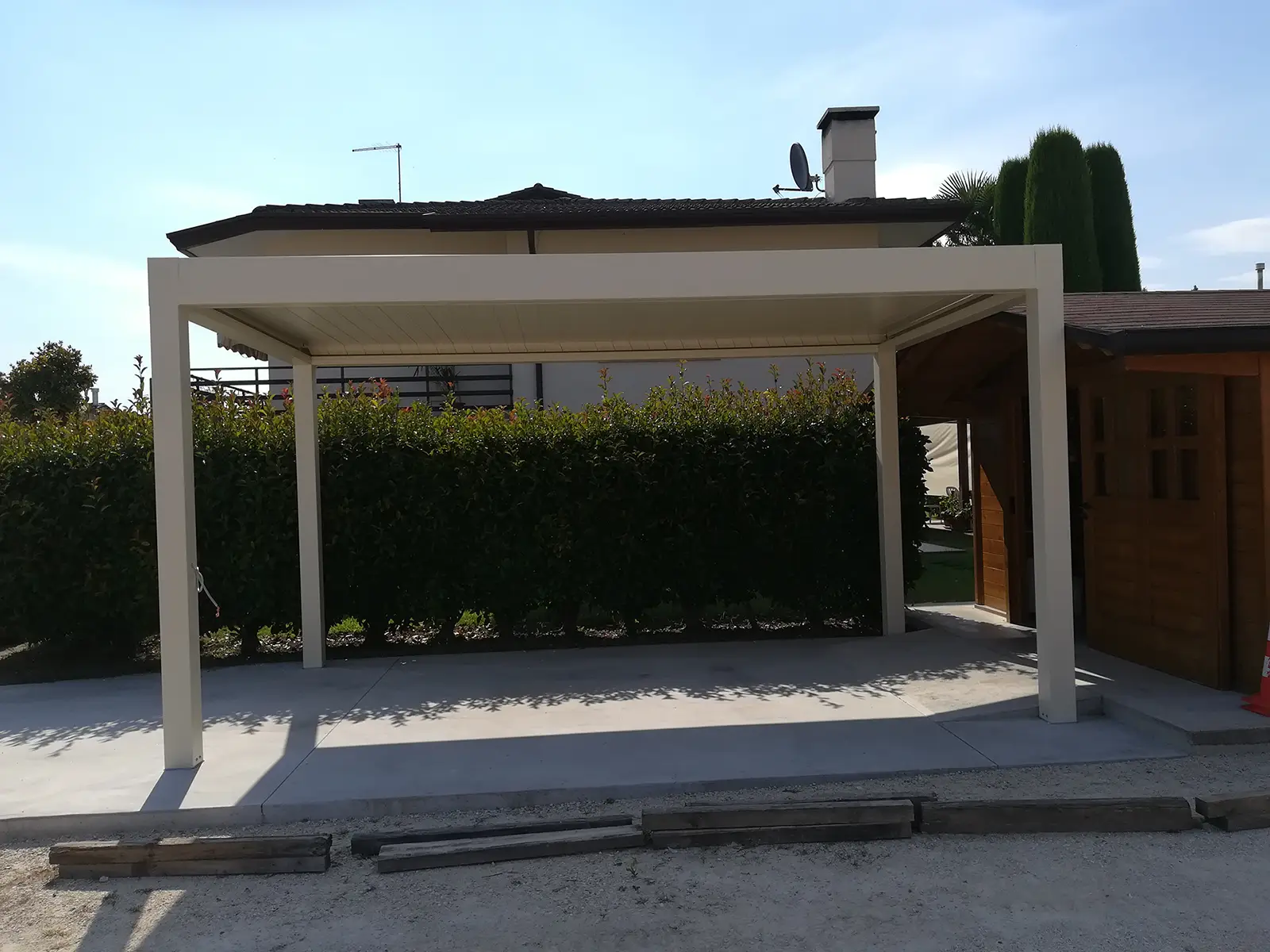 Pergola bioclimatica orientabile 4.0 su cemento adiacente alla siepe